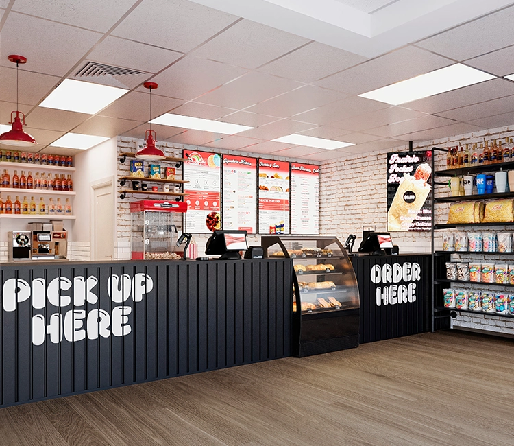 Modern food counter with "Order Here" and "Pick Up Here" signs, showcasing a menu, baked goods, and a variety of beverages on display.